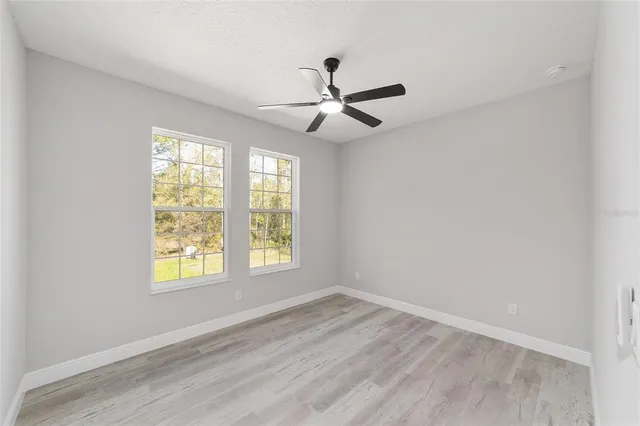 an empty room with wooden floor ceiling fan and windows