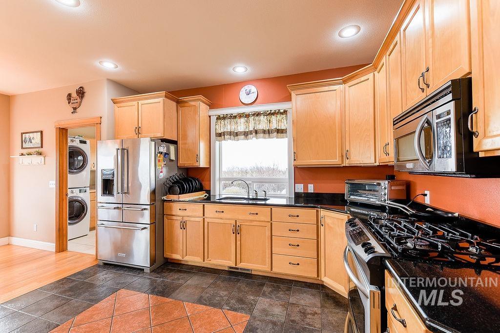 18072 Central Grd Genesee, ID 83832 - Photo 16 of 50 Kitchen featuring stainless steel appliances, stacked washer and clothes dryer, light brown cabinetry, dark stone countertops, and recessed lighting