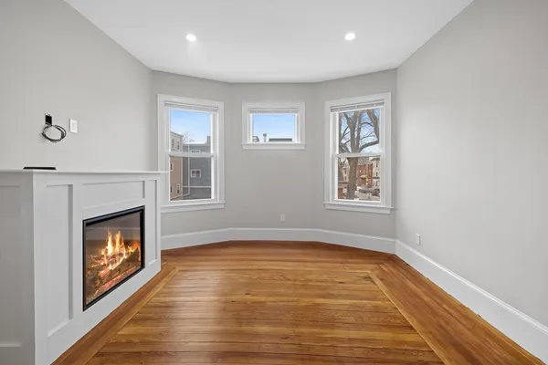 a view of an empty room with wooden floor fireplace and a window