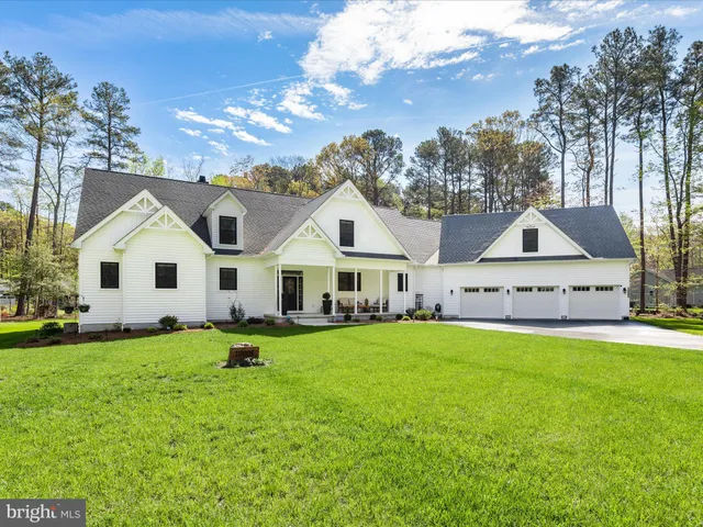 a view of a white house in front of a big yard with plants and large trees