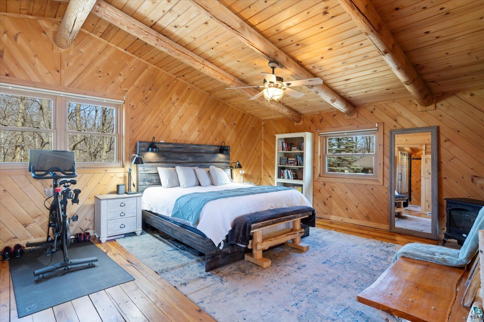717 Bourgin Road Virginia, MN 55792 - Photo 29 of 47 Bedroom with light wood finished floors, wood walls, wooden ceiling, a wood stove, and ceiling fan