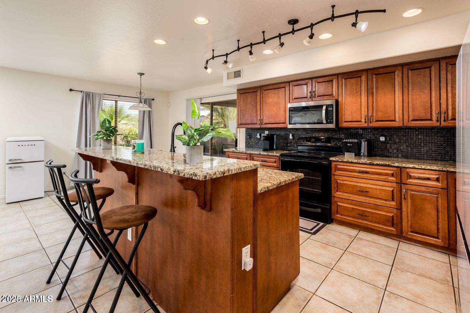 13604 West Rovey Avenue Litchfield Park, AZ 85340 - Photo 14 of 33 a kitchen with stainless steel appliances kitchen island granite countertop a stove a sink and a microwave