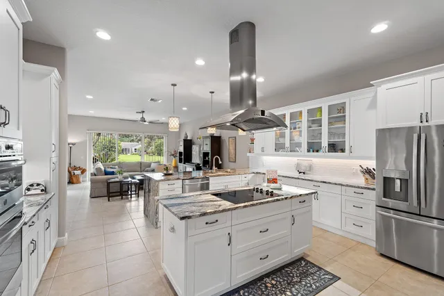 a kitchen with stainless steel appliances kitchen island granite countertop a refrigerator oven a sink dishwasher and white cabinets with wooden floor