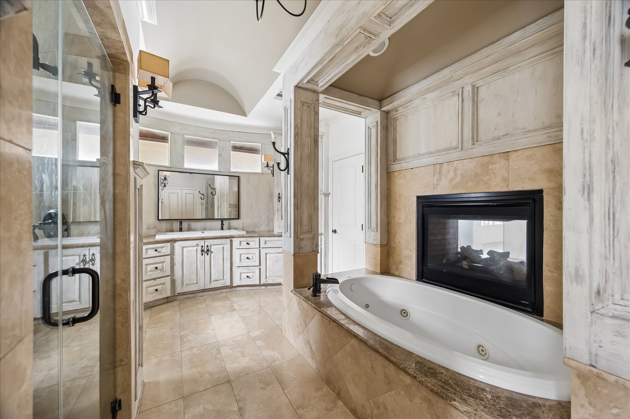 2246 Branard Street Houston, TX 77098 - Photo 27 of 40 An elegant primary bath featuring a soaking tub with dual-sided fireplace, travertine finishes, dual vanities, and custom millwork throughout.