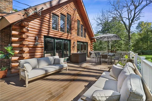a view of a patio with couches table and chairs under an umbrella with large trees