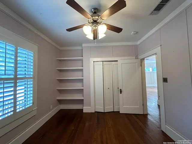a view of an empty room with wooden floor and a chandelier fan