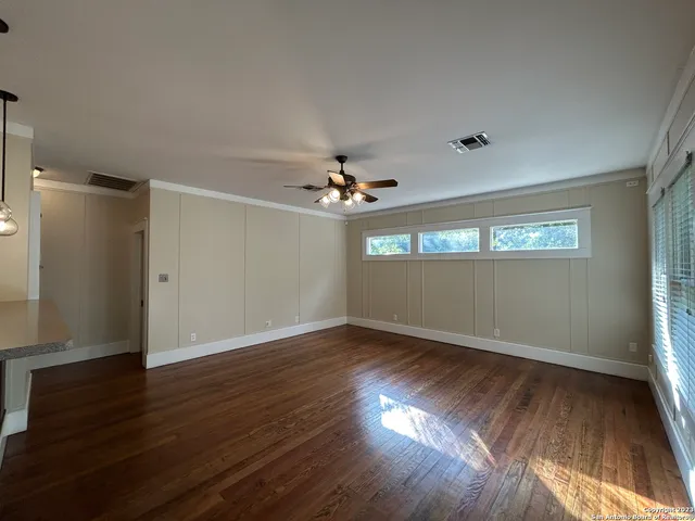 an empty room with wooden floor chandelier fan and windows