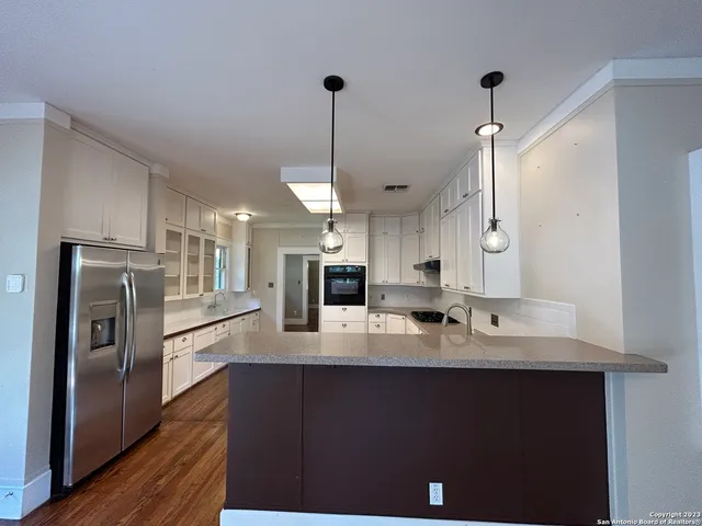 a large kitchen with stainless steel appliances kitchen island granite countertop a refrigerator a stove a sink dishwasher and white cabinets with wooden floor