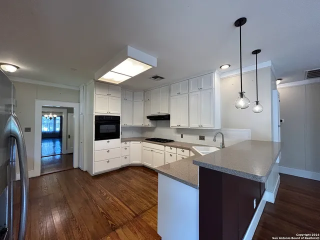a large kitchen with granite countertop a stove top oven a sink dishwasher and white cabinets with wooden floor