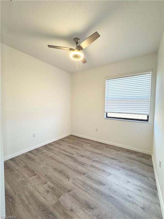 8984 Madrid Circle Naples, FL 34104 - Photo 14 of 28 an empty room with wooden floor ceiling fan and windows