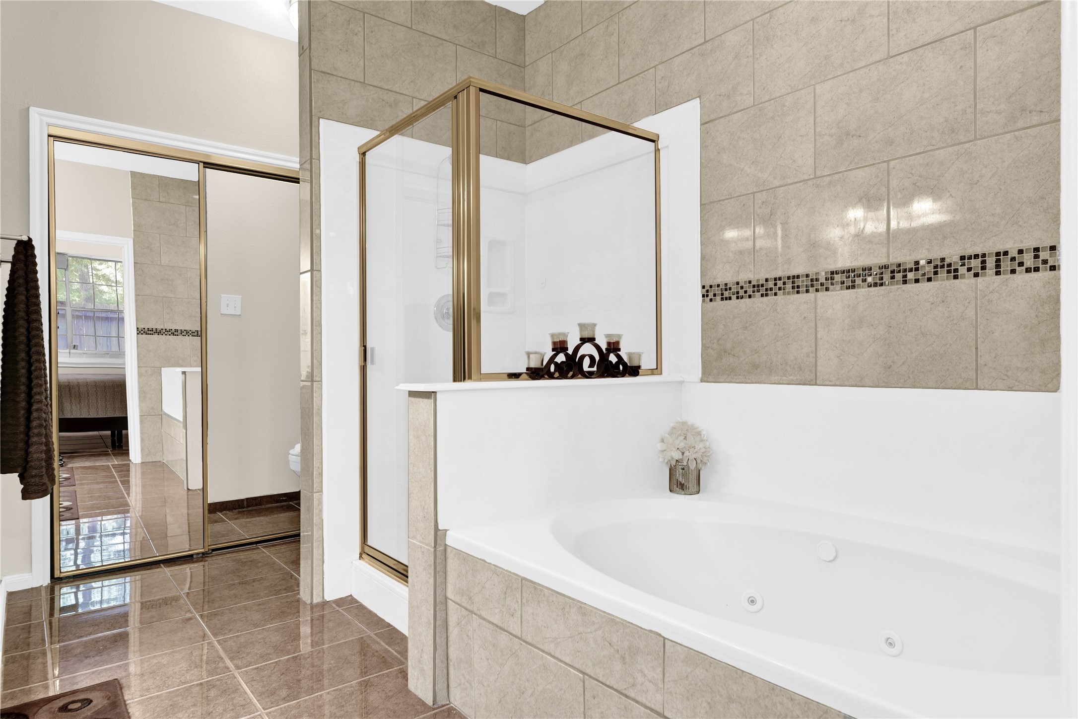 14420 Walters Road, Unit 16 Houston, TX 77014 - Photo 15 of 27 This bathroom features a spacious corner bathtub, a separate glass-enclosed shower, and elegant tilework with decorative accents. The large mirrored closet and natural light add to its modern appeal.