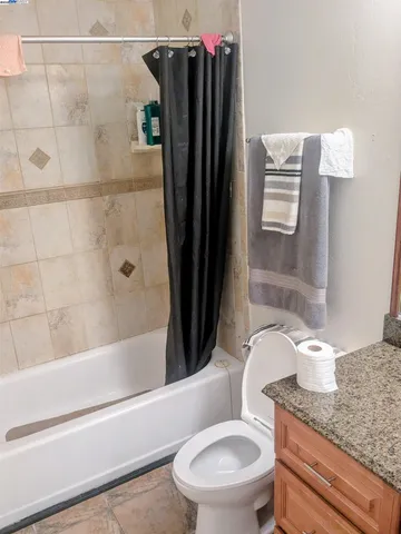 a bathroom with a granite countertop bathtub shower sink vanity and toilet