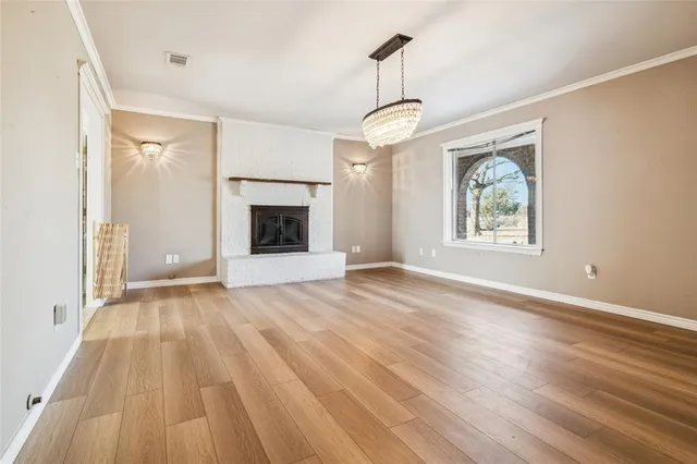 a view of an empty room with wooden floor fireplace and a window