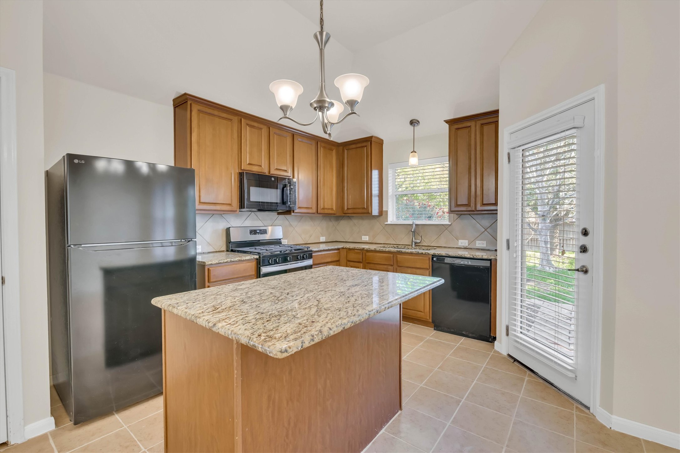 18420 Masi Loop Pflugerville, TX 78660 - Photo 11 of 33 Kitchen featuring wood-finish cabinetry, granite countertops, tile flooring, a central island, and a door with integrated blinds providing outdoor access