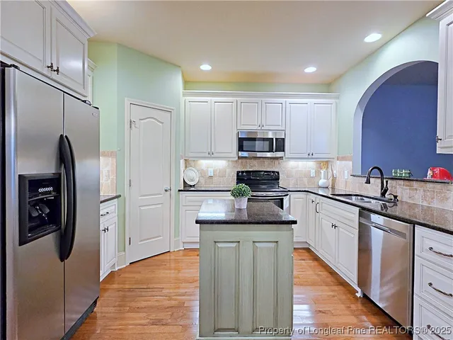 a kitchen with kitchen island granite countertop stainless steel appliances cabinets a sink and a refrigerator