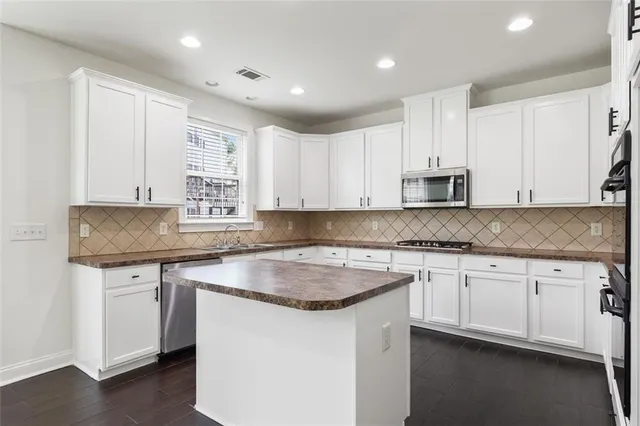 a kitchen with stainless steel appliances granite countertop a sink a stove a white refrigerator and white cabinets