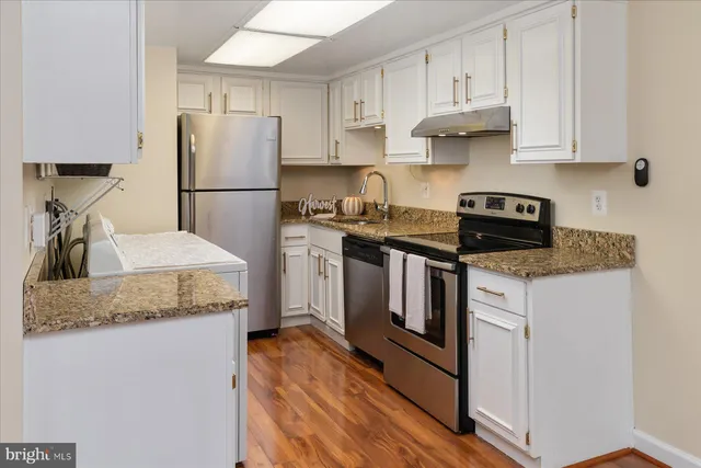 a kitchen with stainless steel appliances granite countertop a refrigerator sink stove and white cabinets