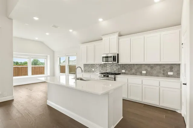 a large kitchen with stainless steel appliances granite countertop a stove a sink a refrigerator and white cabinets with wooden floor