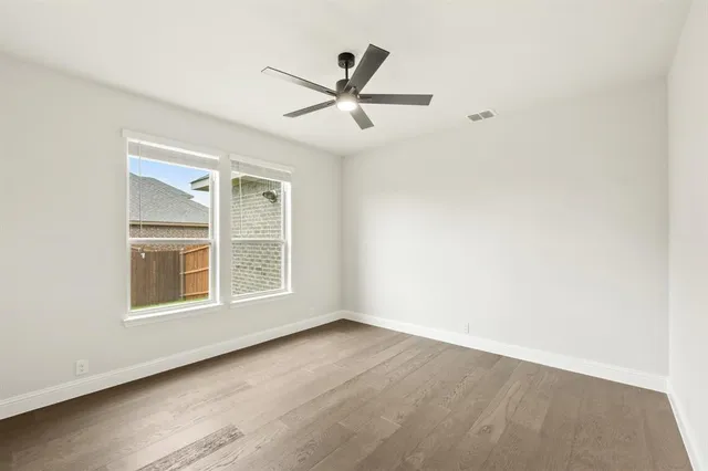 an empty room with wooden floor ceiling fan and windows