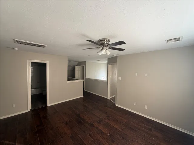 a view of an empty room with wooden floor and a ceiling fan