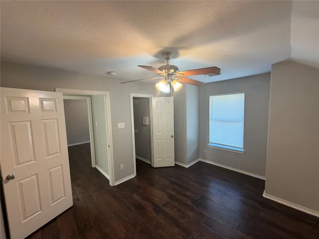 a view of an empty room with wooden floor and a ceiling fan