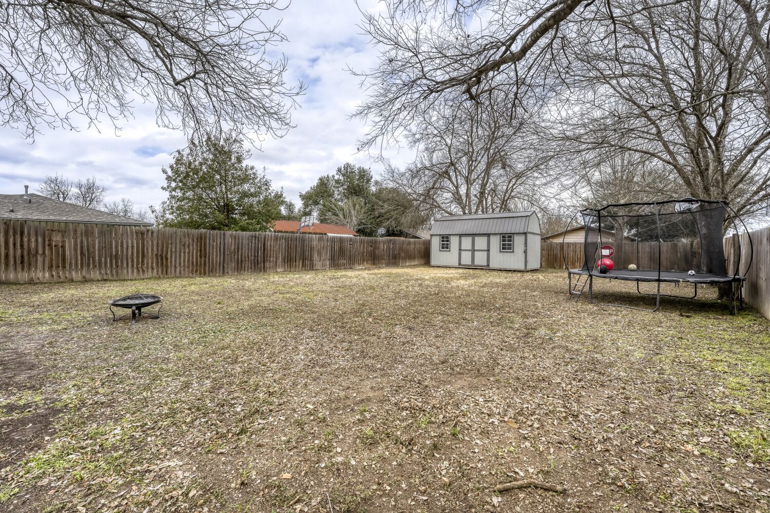 125 Irene Street Elgin, TX 78621 - Photo 20 of 24 Fenced backyard with a fire pit, a storage unit, and a trampoline