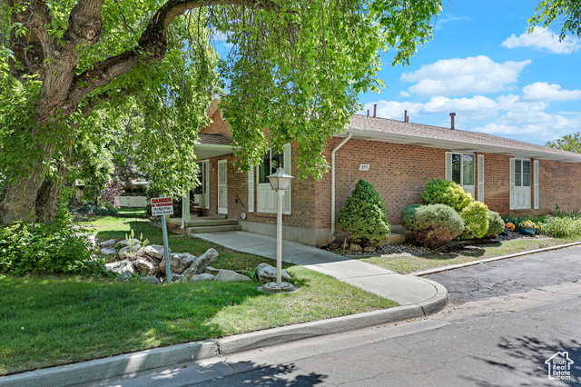 View of property hidden behind natural elements featuring brick siding, a front lawn, and a shingled roof