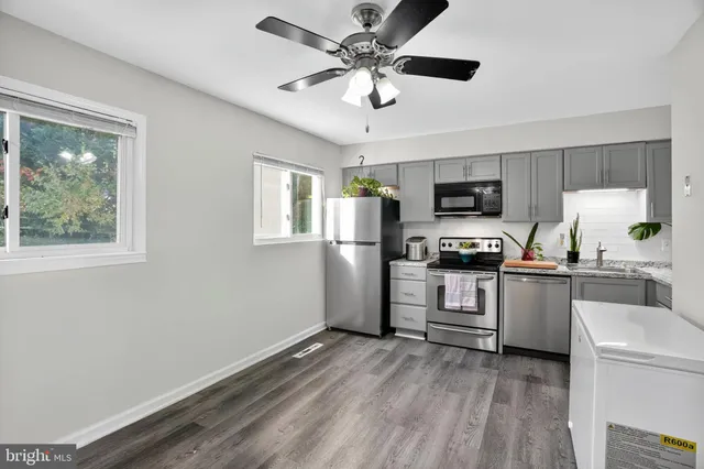 a kitchen with granite countertop a refrigerator a stove a microwave oven a sink dishwasher and white cabinets with wooden floor