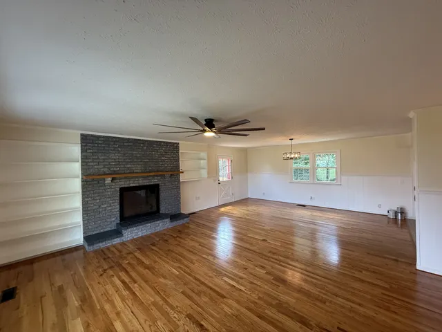 an empty room with wooden floor fireplace and windows