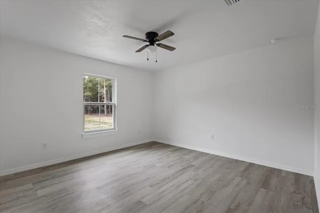 an empty room with wooden floor chandelier fan and windows