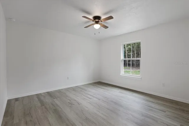 an empty room with wooden floor chandelier fan and windows