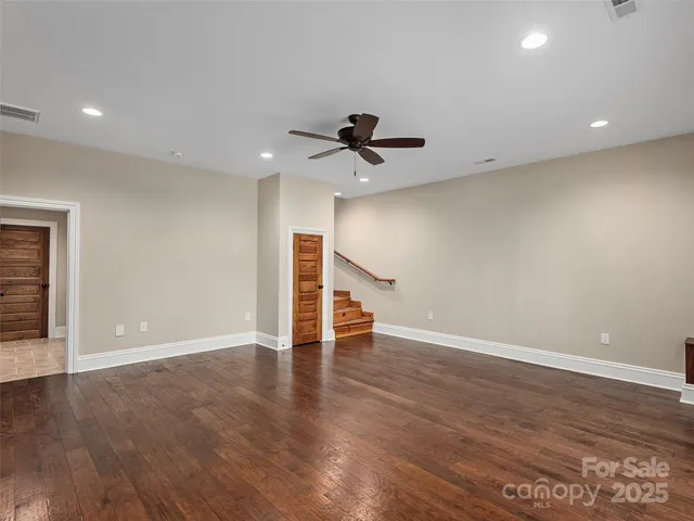 a view of an empty room with wooden floor and a ceiling fan