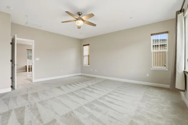 an empty room with chandelier fan and windows