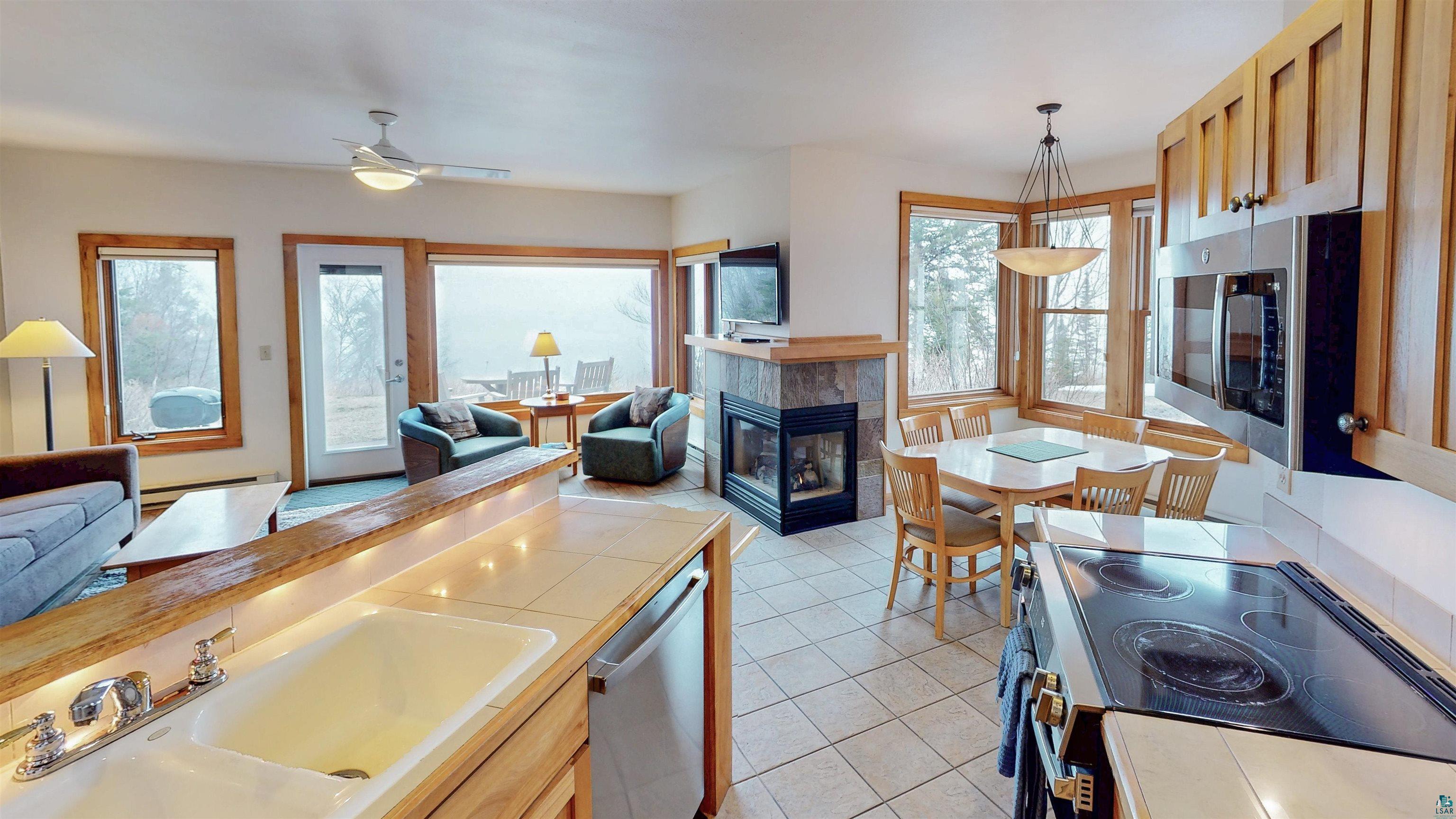 504-506 Poplar River Road, Unit 505 Lutsen, MN 55612 - Photo 8 of 39 Open-concept living space featuring a built-in tiled fireplace, wood-frame windows, a dining area with a chandelier, a kitchen with wood cabinetry and stainless steel appliances, and tiled flooring