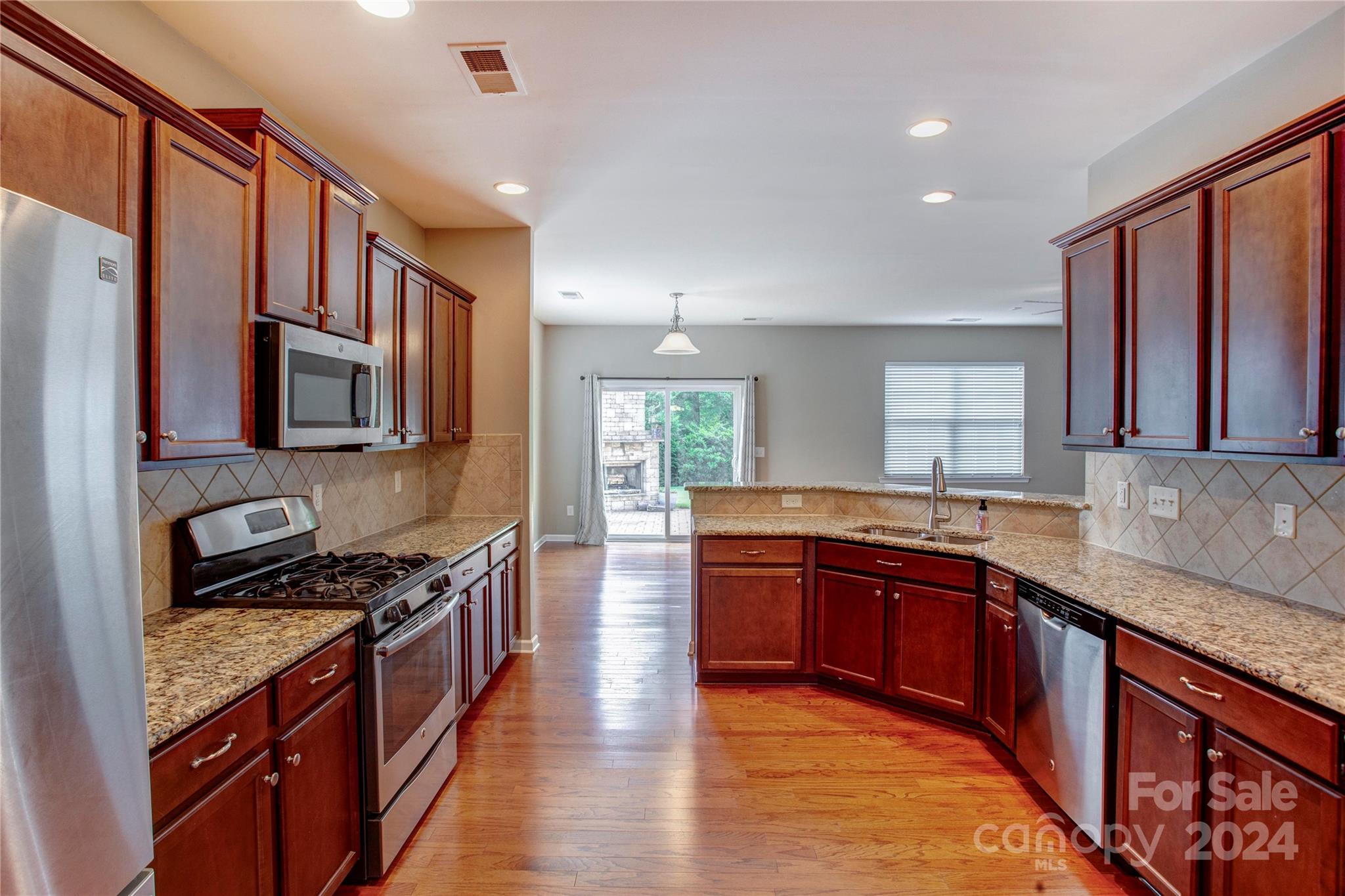 8899 Happiness Road Harrisburg, NC 28075 - Photo 6 of 30 a large kitchen with stainless steel appliances granite countertop a stove top oven a sink dishwasher a dining table and chairs with wooden floor