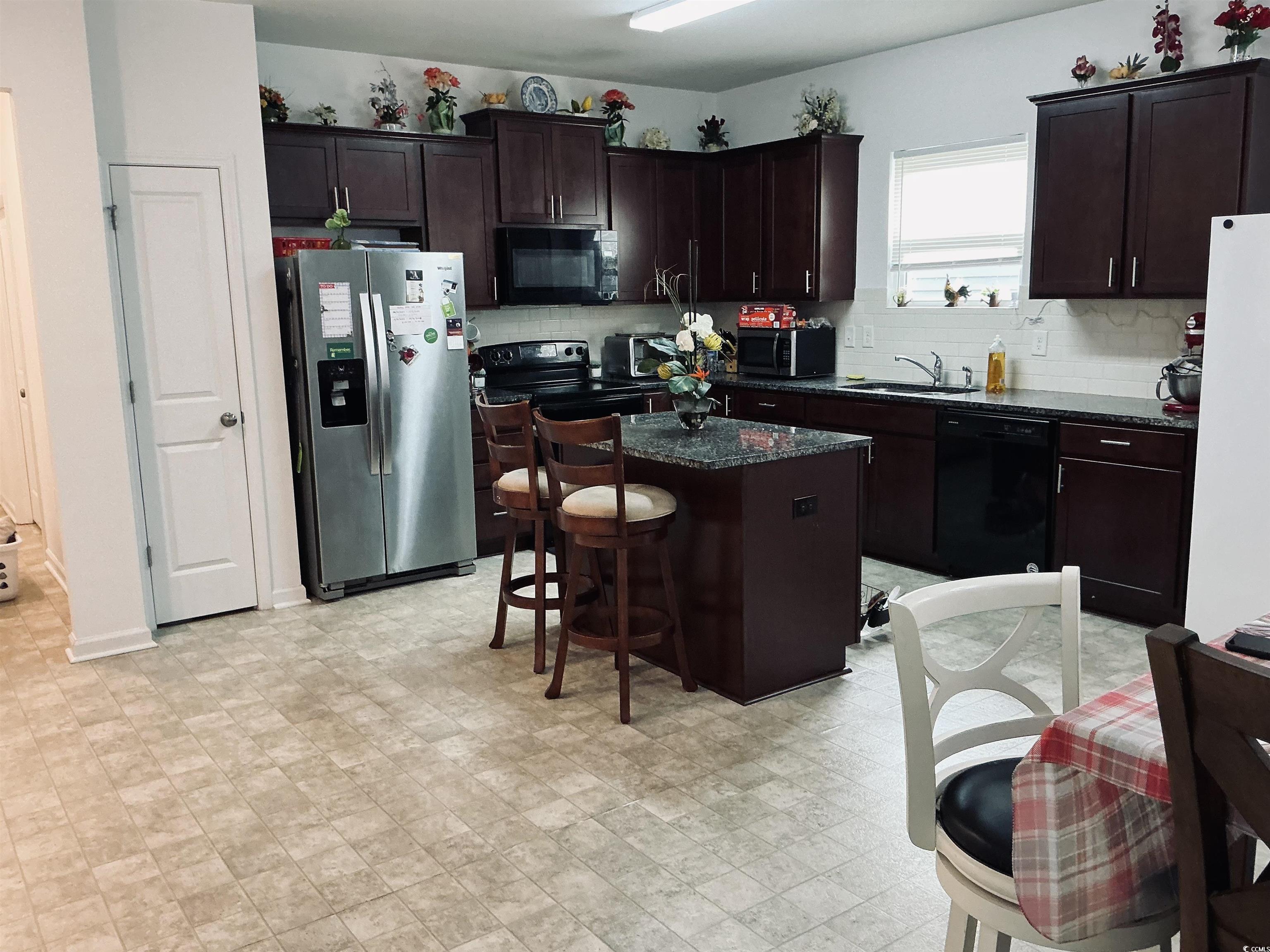 5260 Walnutwood Trail Myrtle Beach, SC 29579 - Photo 11 of 30 Kitchen with dark brown cabinetry, black appliances, a center island, a kitchen breakfast bar, and dark stone countertops