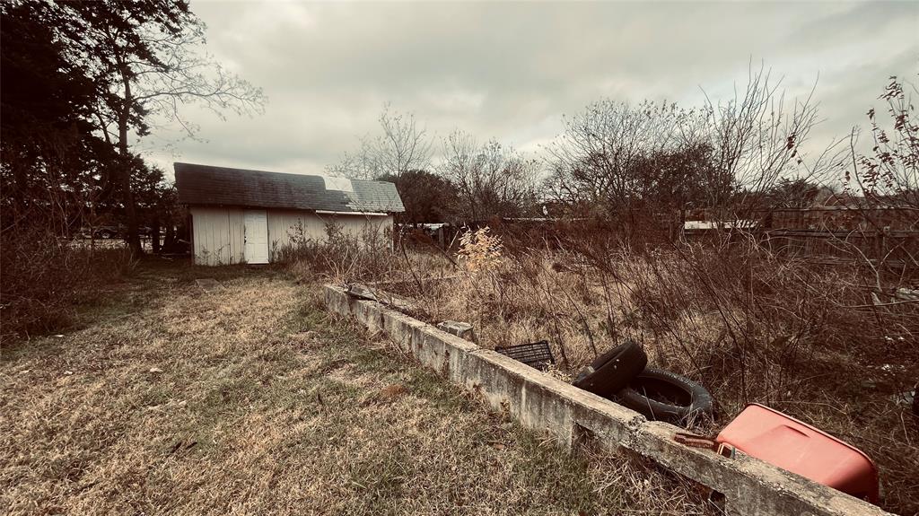 1445 Elk Creek Road Dallas, TX 75253 - Photo 3 of 4 Backyard view with overgrown vegetation, concrete divider, and small detached outbuilding. Area contains debris and tires, indicating need for full cleanup.