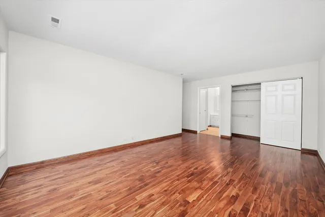 a view of an empty room with wooden floor and closet