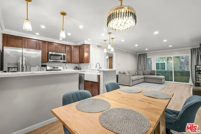 a kitchen with stainless steel appliances kitchen island granite countertop a sink dishwasher a stove a refrigerator with a dining table and chairs with wooden floor