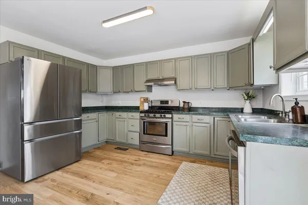 a kitchen with stainless steel appliances a dining table chairs refrigerator and wooden floor