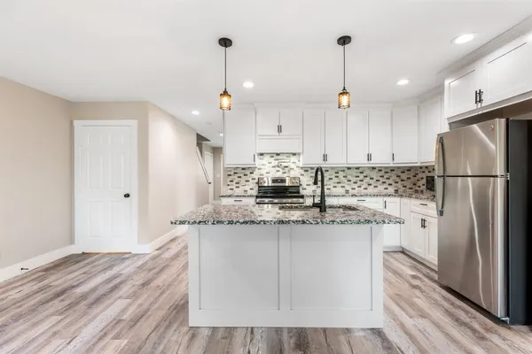 a kitchen with stainless steel appliances granite countertop a refrigerator a sink dishwasher a stove and white cabinets with wooden floor