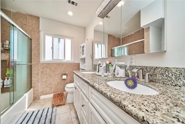 a bathroom with a granite countertop sink a toilet a mirror and shower