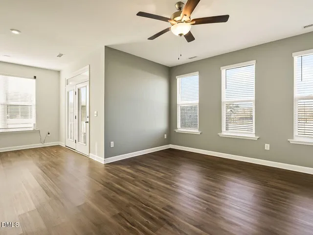 a view of an empty room with wooden floor and a ceiling fan