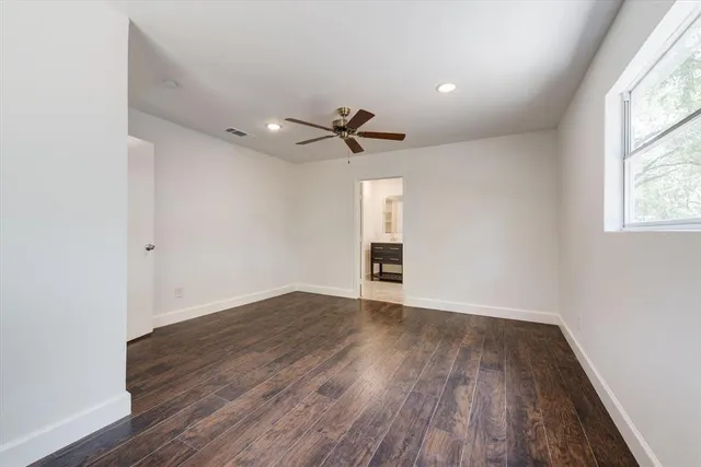 a view of an empty room with wooden floor and a ceiling fan