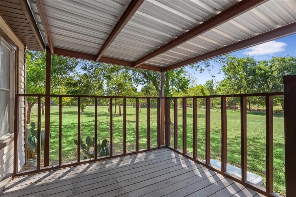 4246 Old Caufield Ranch Road McGregor, TX 76657 - Photo 20 of 31 Covered porch with wood decking, metal roof, and wood railings overlooking a grassy expanse with mature trees