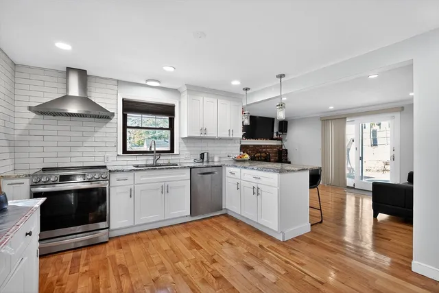 a kitchen with stainless steel appliances kitchen island granite countertop a stove top oven a sink a dining table and chairs with wooden floor