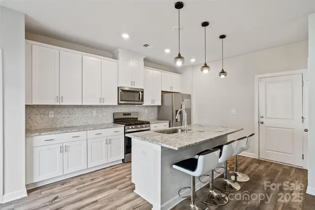 a kitchen with stainless steel appliances granite countertop a stove a sink a refrigerator a white table and chairs with wooden floor