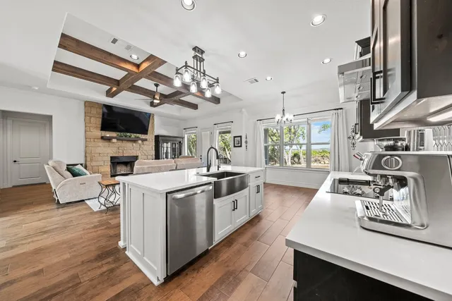 a open kitchen with stainless steel appliances granite countertop a stove top oven a sink dishwasher and white cabinets with wooden floor