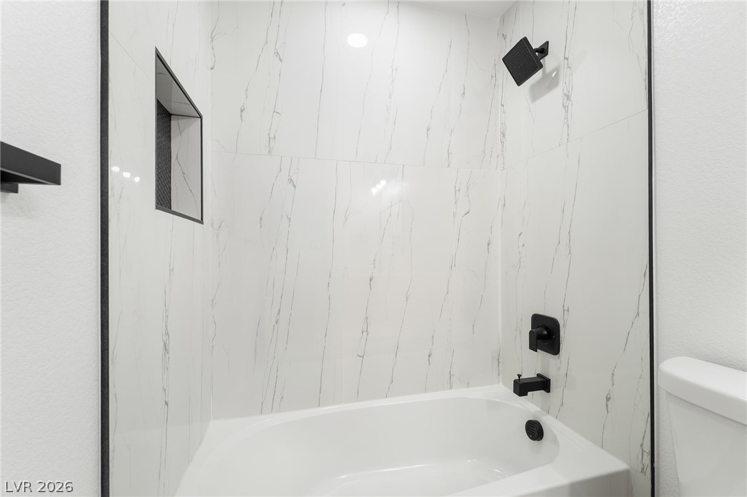 39 Lowery Street Henderson, NV 89015 - Photo 23 of 40 A pristine bath and shower area features modern matte black fixtures against elegant white marble-patterned tile.