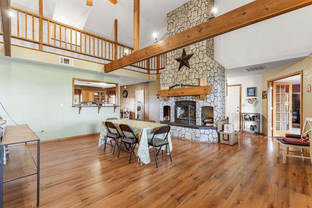 13315 Highway 281 Scotland, TX 76379 - Photo 7 of 40 Spacious great room featuring a vaulted ceiling with exposed wood beams, a stone-clad fireplace with wood mantle, parquet flooring, a kitchen pass-through window with a bar, and a second-story loft